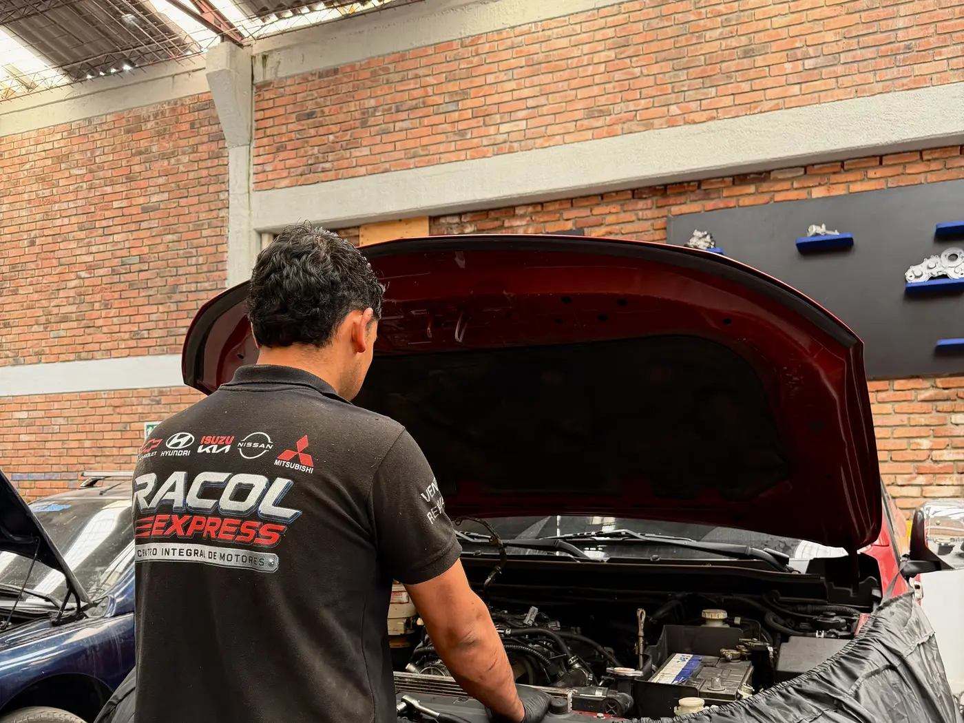 Un mecánico de RACOL EXPRESS trabajando en el motor de un carro con el capó abierto, en el taller