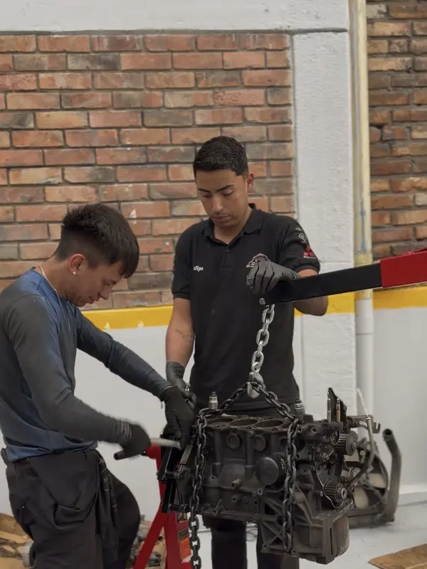 Dos mecánicos montando un bloque de motor en el soporte